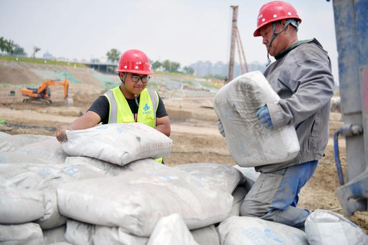 6月26日上午,施工员王志(左)正帮着建筑工人堆放水泥