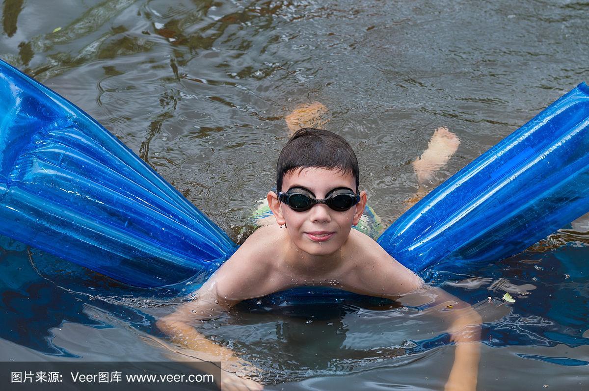 男孩在河里的蓝色床垫上游泳