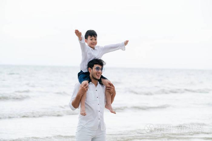 快乐的父亲在夏天的热带沙滩上背着儿子的脖子上