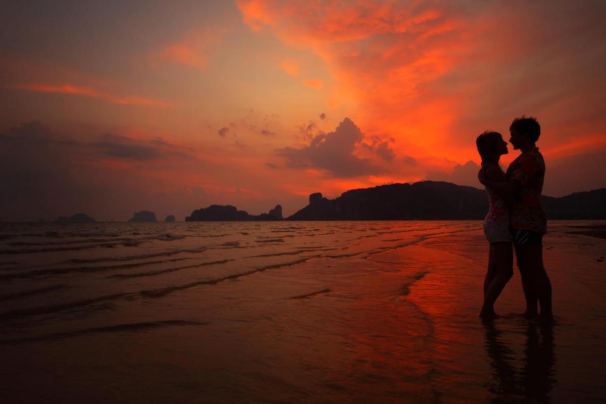 两个年轻的恋人站在湿海滩上和日落背景上拥抱幸福情侣图片