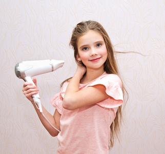 可爱的微笑着的小女孩用吹风机把她的长发擦干照片