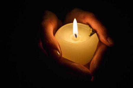 燃烧蜡烛在一个祈祷的女孩在一个黑色的背板上的手中照片