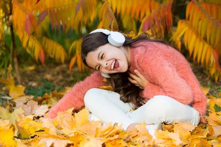 小女孩戴着耳机在秋树旁放松.音乐为愉快舒适的心情.