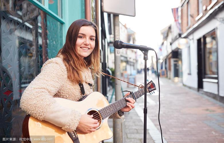 年轻女音乐家的肖像街头演奏原声吉他和在街头户外唱歌