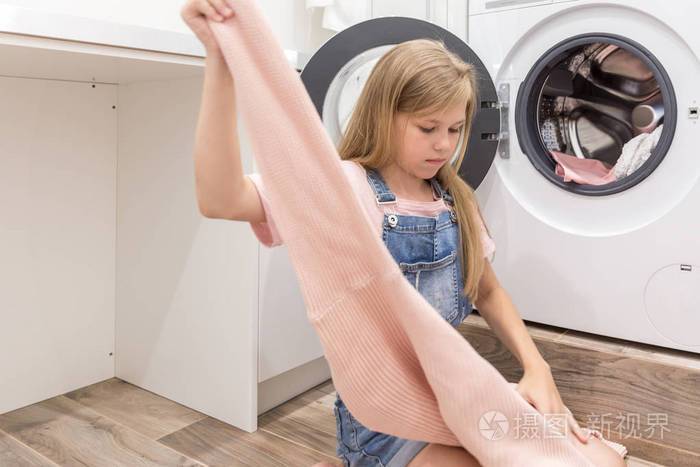 幸福家庭的母亲家庭主妇和孩子的女儿在洗衣房里用洗衣机和衣服