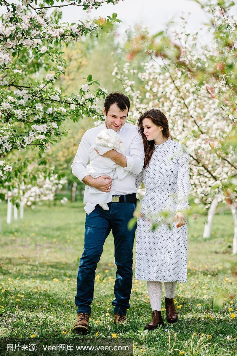 年轻美丽的一家人抱着小宝宝在苹果园里互相拥抱.