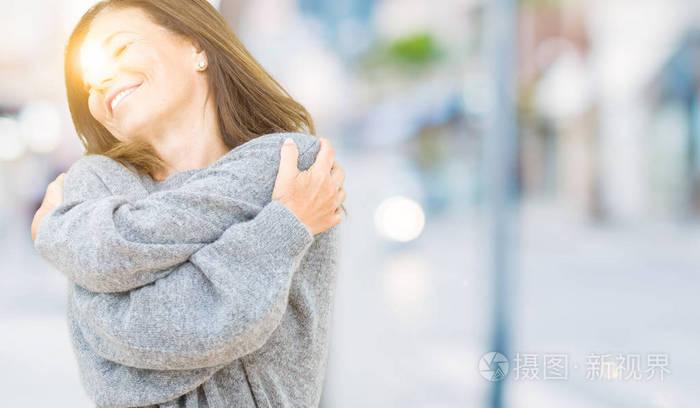 美丽的中年妇女穿着冬天的毛衣,在孤立的背景下拥抱自己,快乐而积极的