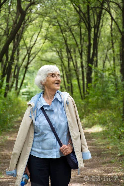 快乐的老年妇女在夏天的绿色公园散步