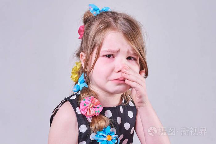 一个美丽的小女孩, 带着悲伤的表情, 哭着, 用双手拭去泪水.