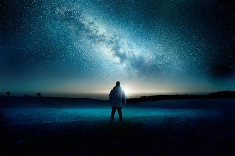 当月亮和银河的银河填满夜空时, 一个男人站在那里, 惊奇而惊异地注视