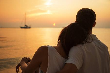 大海船之路下浪漫的肖像,迷人的夫妇在爱情拥抱坐在海滩上的夕阳在