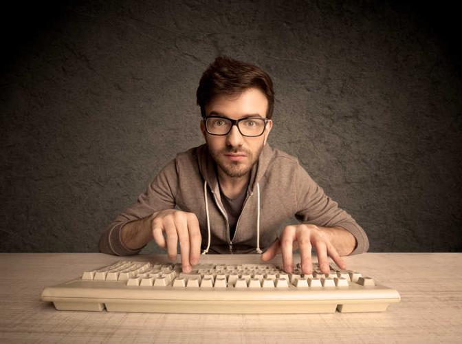 灰色背景下木桌上的双手在键盘上打字的男人