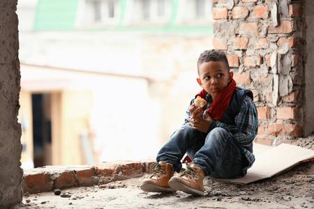 可爱的小男孩坐在地板上片面包在废弃的建筑.贫困的概念照片