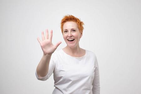 牛排五成熟相当成熟的女人与红色的头发在白色 t恤显示5或五手指手势.