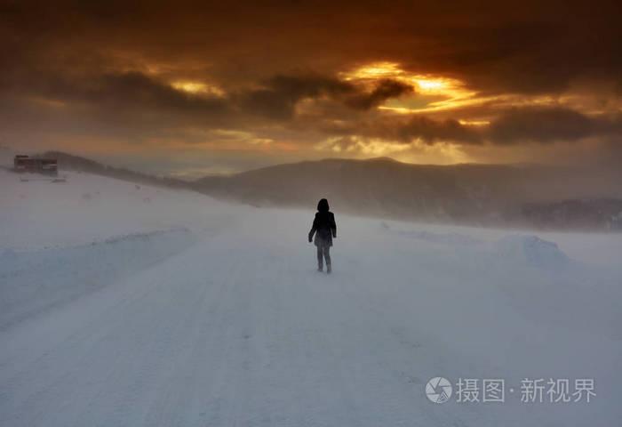 日落时分独自在暴风雪中行走的女人