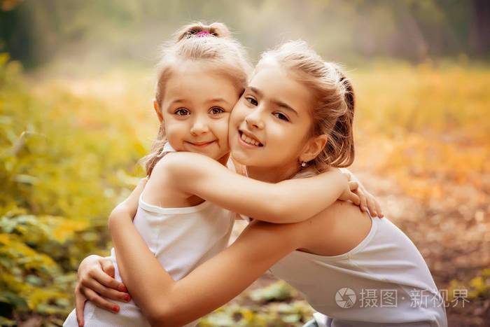 童年,亲情, 友情和人们观念-两人开心的孩子拥抱在户外的姐妹