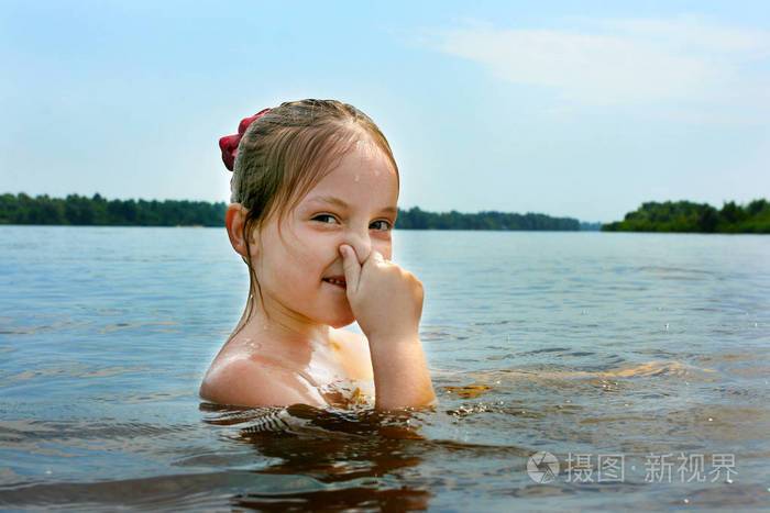 一个湿头可爱的小女孩在河里游泳她用手pinchs她的鼻子