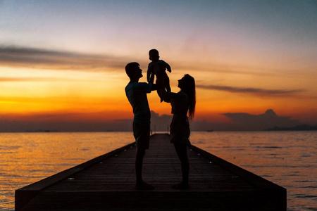 一家人在夕阳下拥抱着儿子,剪影.照片