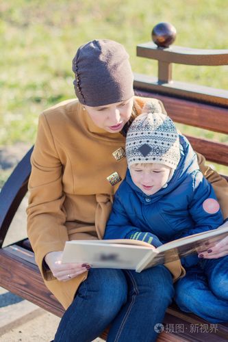 年轻女人和小男孩坐在板凳上,在秋天公园和看书.家人在一起享受时光.