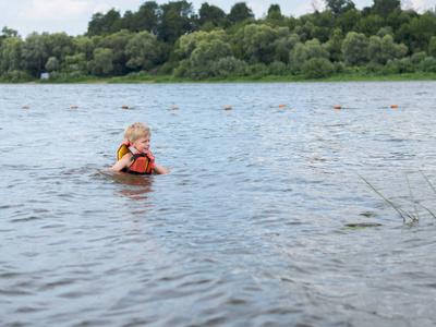 可爱的小男孩在橙色生活背心游泳在河里照片