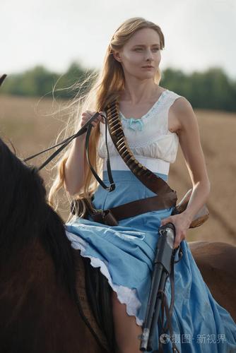 一个美丽的女子女牛仔与猎枪从野生西部骑马在内陆的画像