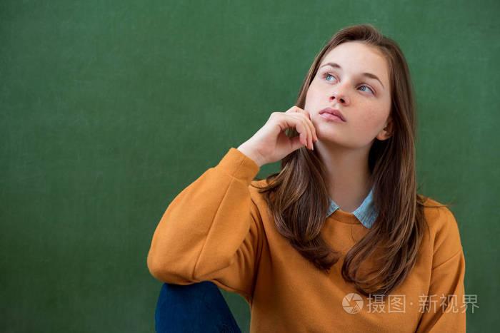 学生思考并倾向于绿色黑板背景. 沉思的女孩抬头看. 高加索女学生肖像