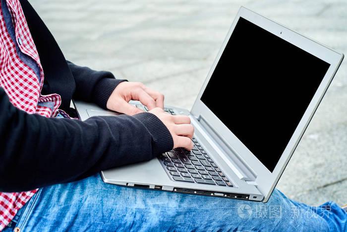 侧面观看男子衬衫和牛仔裤打字在笔记本电脑键盘上的khees户外复制