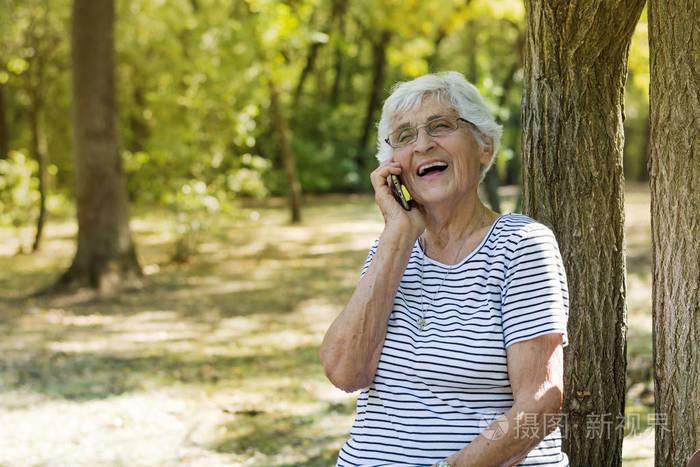 快乐的老年妇女在公园的室外打电话