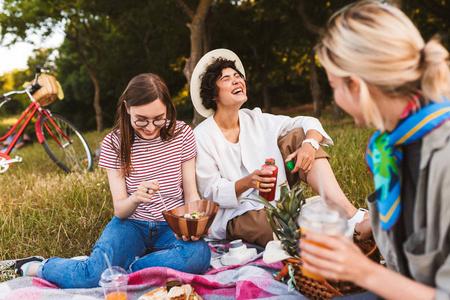 快乐的女孩坐在野餐毯子愉快地笑花时间一起在公园野餐照片