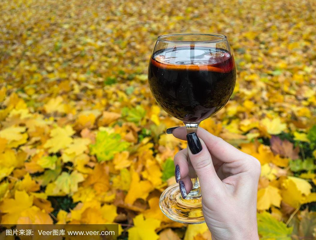 在一个寒冷的秋天,一个女人手里拿着一杯热红酒,背景是黄色和红色的