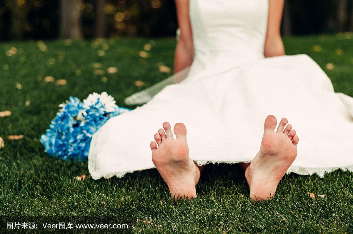 年轻的金发新娘赤脚坐在草地上