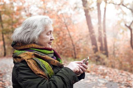 在秋季公园散步的老年妇女用手机照片