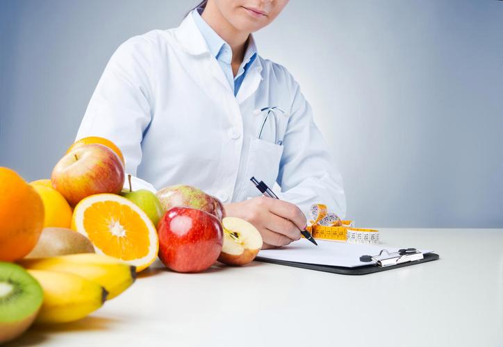 新鲜水果前专业营养师在办公桌前工作和写病历与