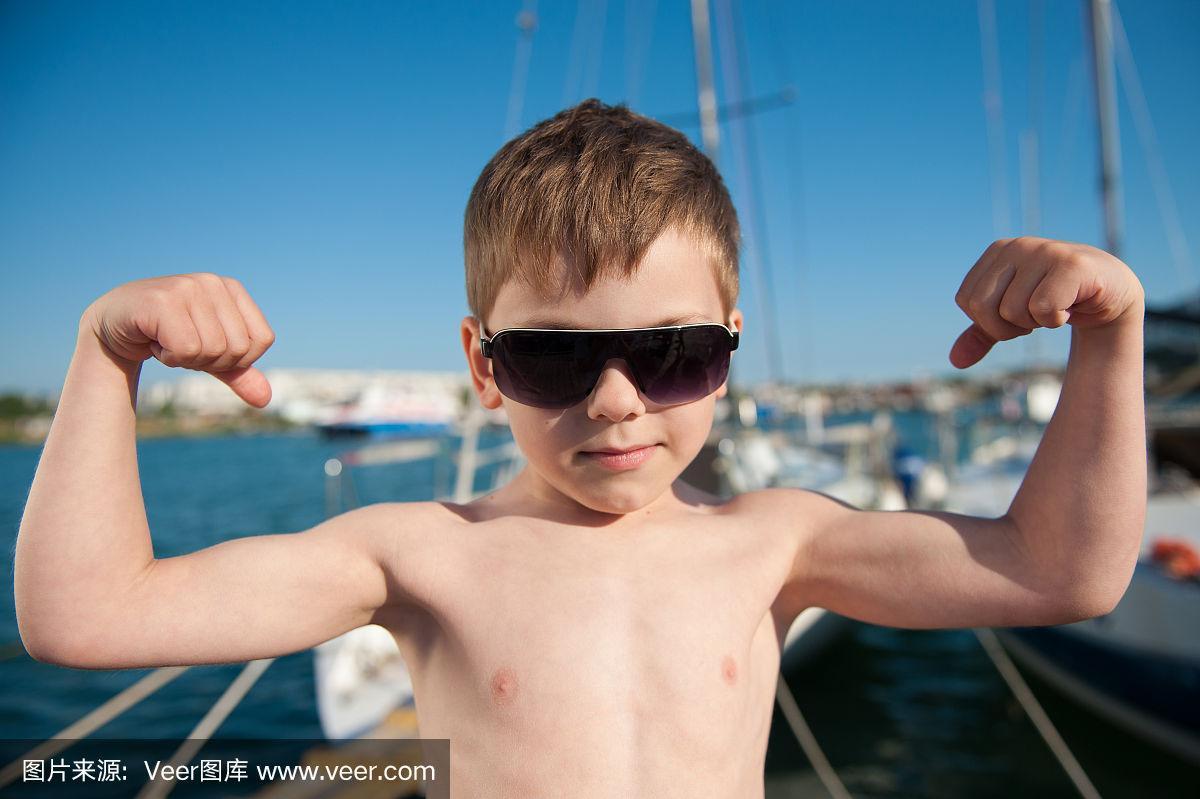 可爱的小男孩戴着太阳镜在夏天展示他的肌肉