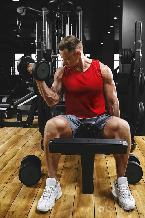 一个赤膊肌肉男正在做二头肌和哑铃练习,作为他的健身锻炼的一部分.