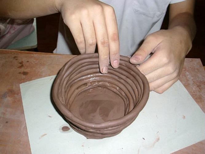 2,用双手搓捻陶泥,使其成为条状,再把搓捻成条状的陶泥捏粘到底部.