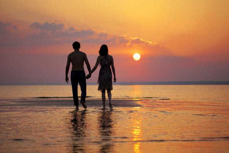 日落时两个相爱的人手牵手散步